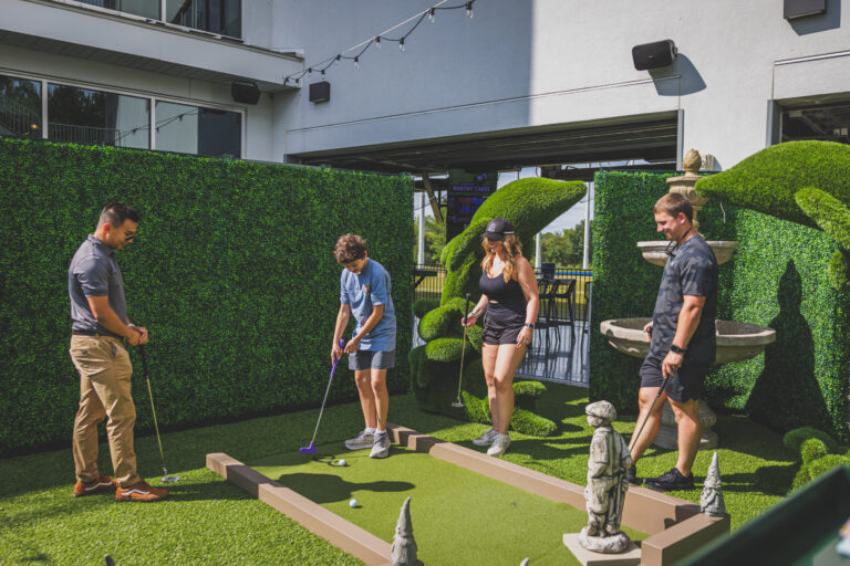 Family enjoying colorful mini golf course at Drive Shack’s Art Garden.